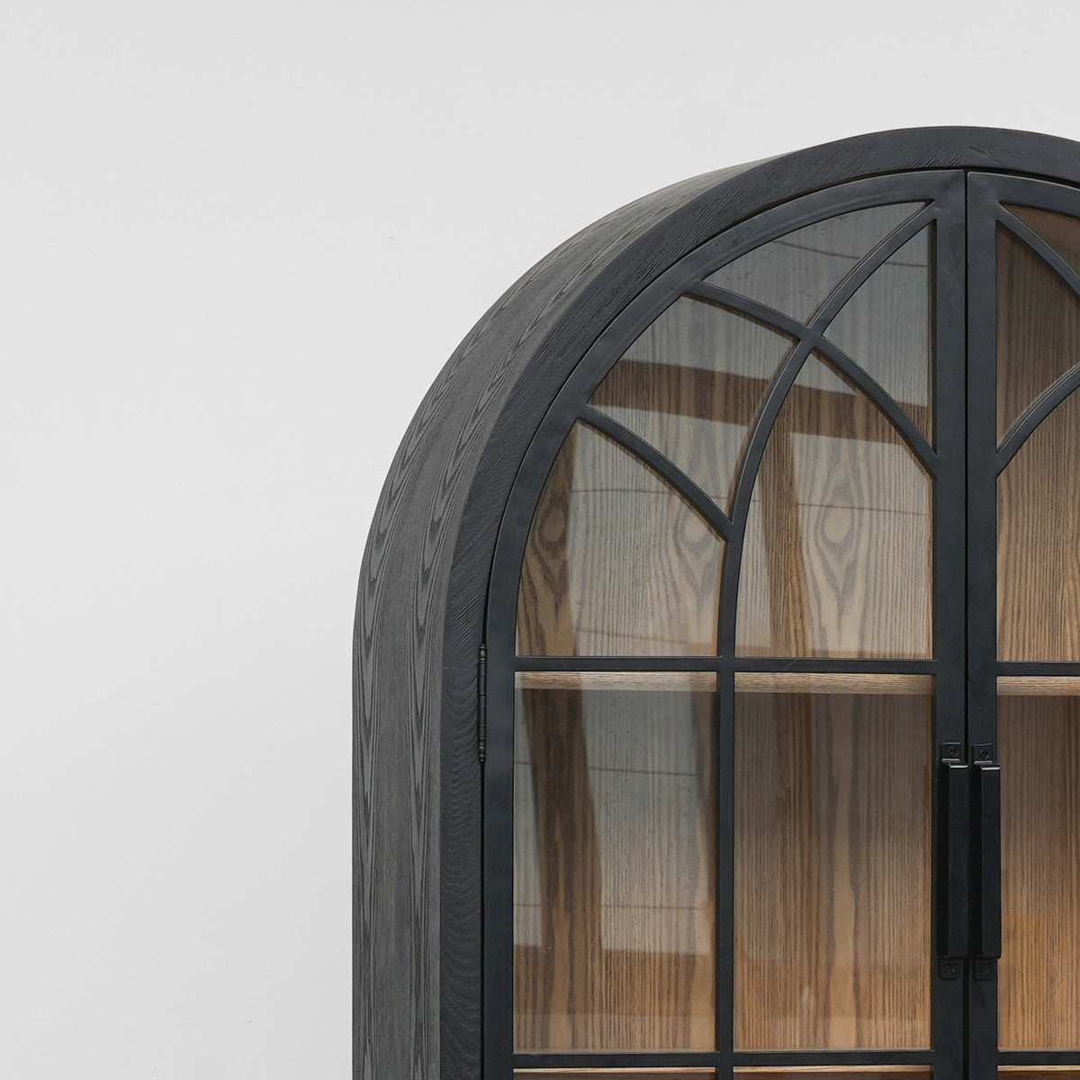 Close-up of arched glazed cabinet doors with black metal framing and dark wood grain, reflecting traditional ecclesiastical architecture.