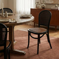 Langford Oak Bistro Chair with solid oak frame, hand-finished rattan back, and cushioned woven seat at a dining table.