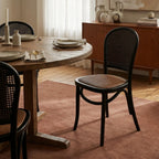 Langford Oak Bistro Chair with solid oak frame, hand-finished rattan back, and cushioned woven seat at a dining table.