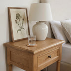 Oakridge Bedside Table in solid oak with framed drawer fronts, turned legs and a lower shelf beside a lamp.