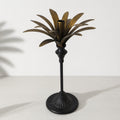 Tall brass palm candle holder with sculptural palm leaves surrounding a central candle cup.