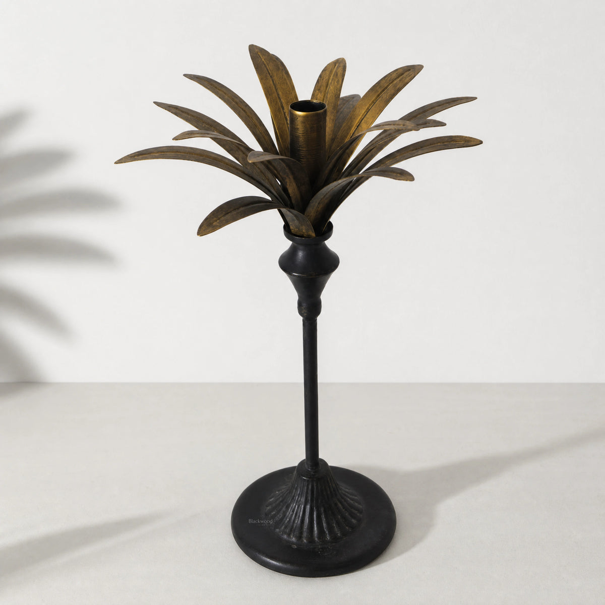 Tall brass palm candle holder with sculptural palm leaves surrounding a central candle cup.