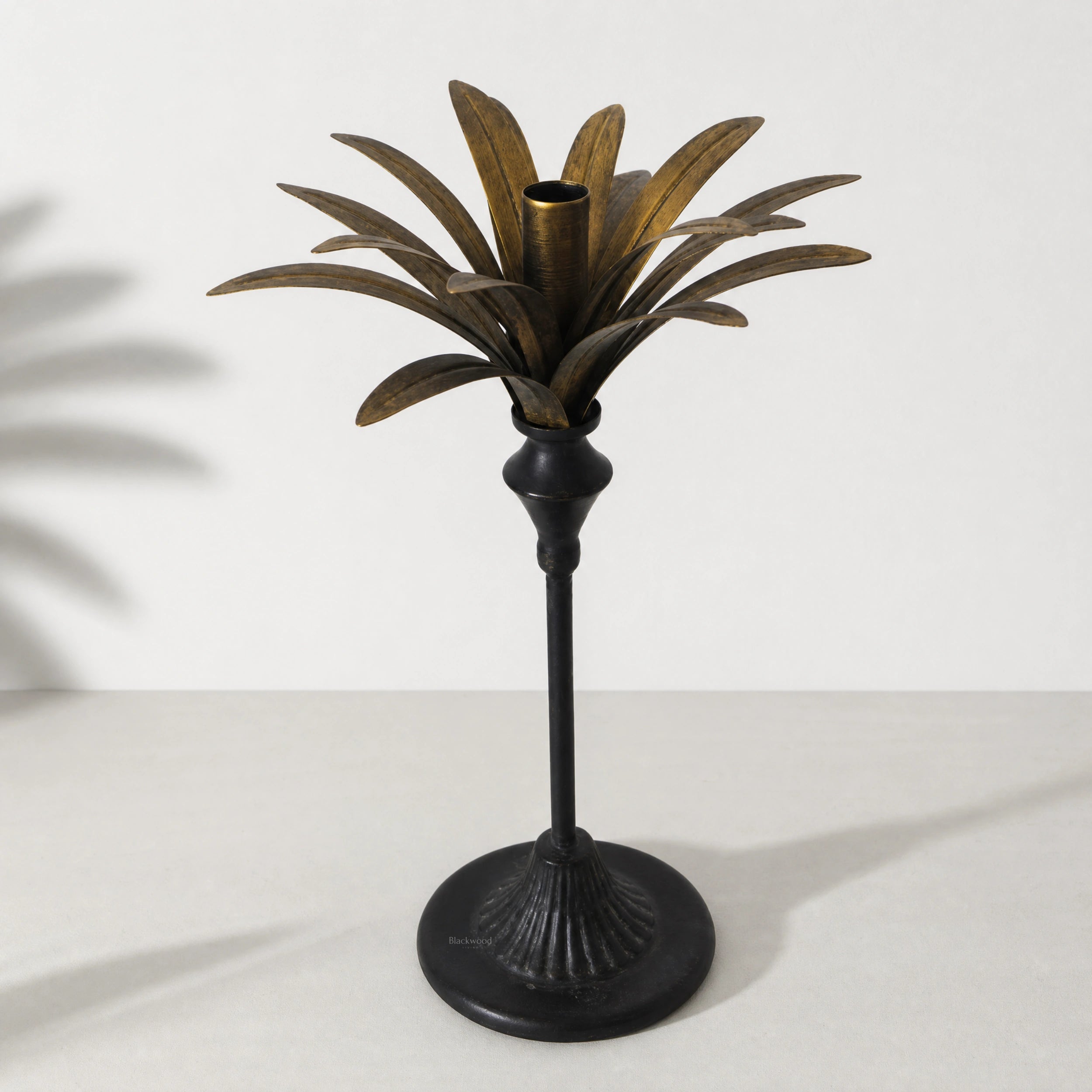 Tall brass palm candle holder with sculptural palm leaves surrounding a central candle cup.