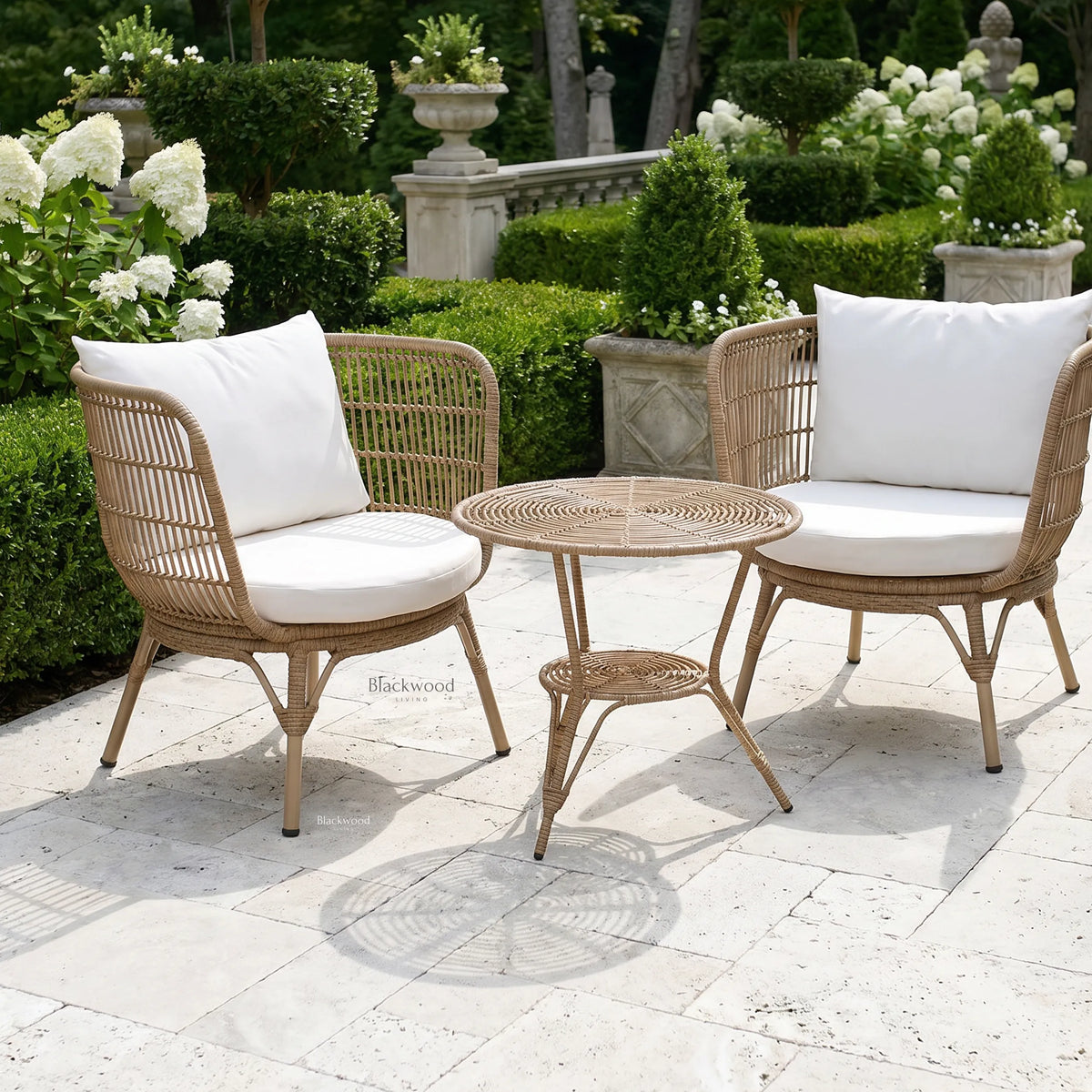 Clifton Outdoor 3-Piece Setting: wicker chairs with white cushions on a stone patio amid lush garden greenery