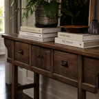 The Raffles Console in aged elm with rich grain, paired with a ceramic planter and stacked books.