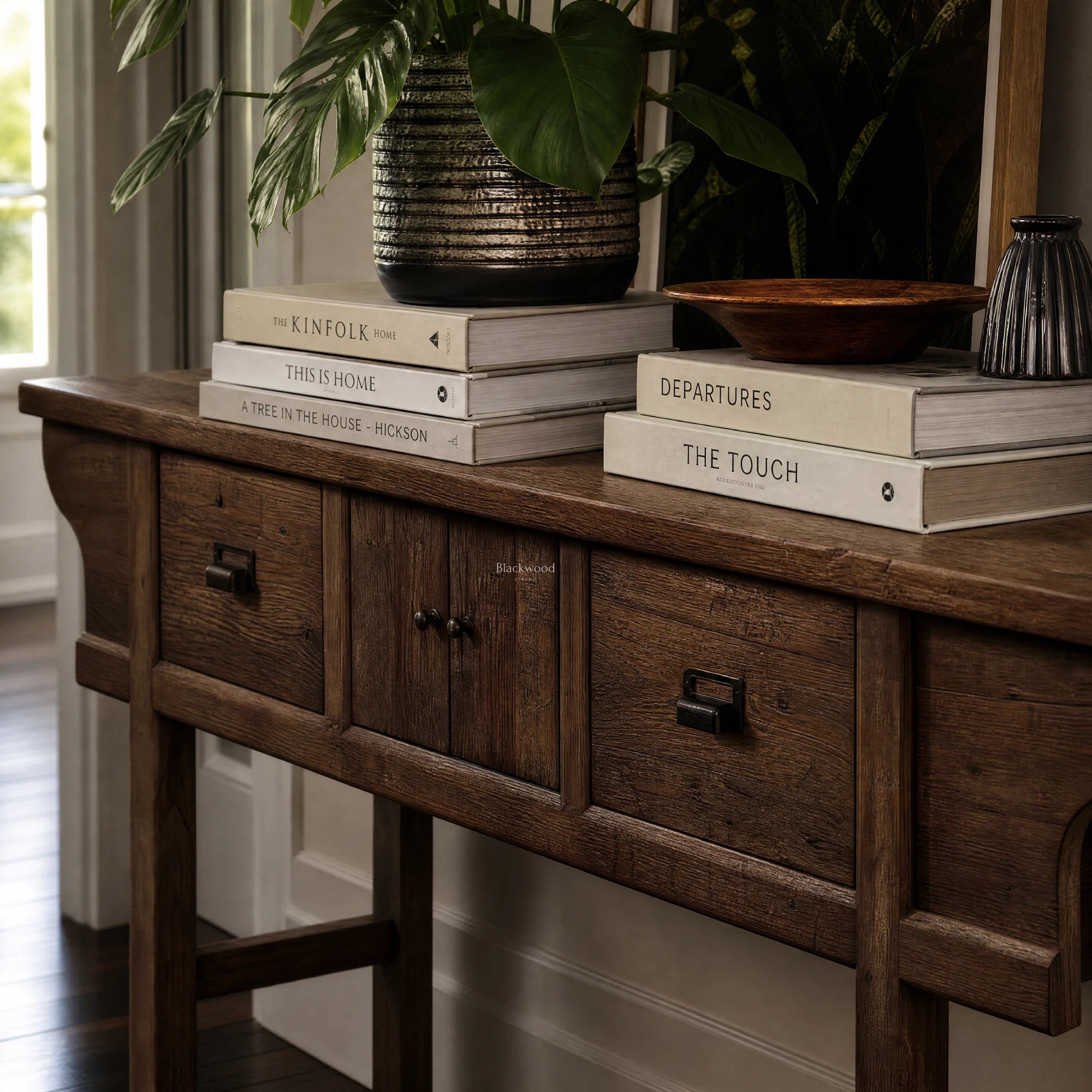 The Raffles Console in aged elm with rich grain, paired with a ceramic planter and stacked books.