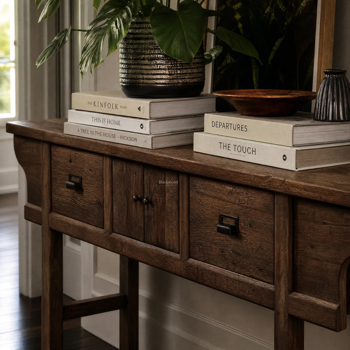 The Raffles Console in aged elm with rich grain, paired with a ceramic planter and stacked books.