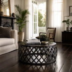 Mara Coffee Table with round iron lattice base in a sunlit living room, topped with books and plants.