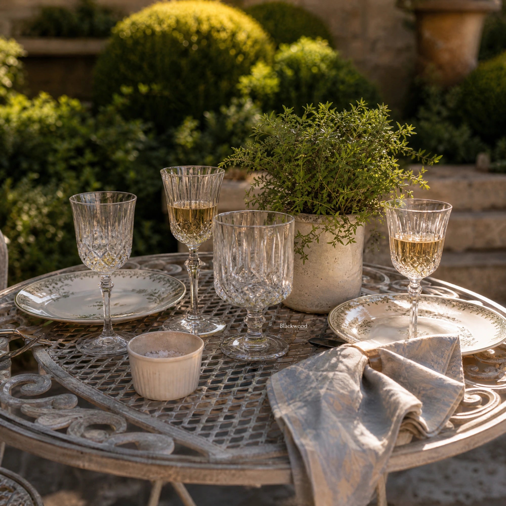Provence Bistro Set in weathered antique-grey with delicate scrollwork, set on a garden table with crystal glasses.
