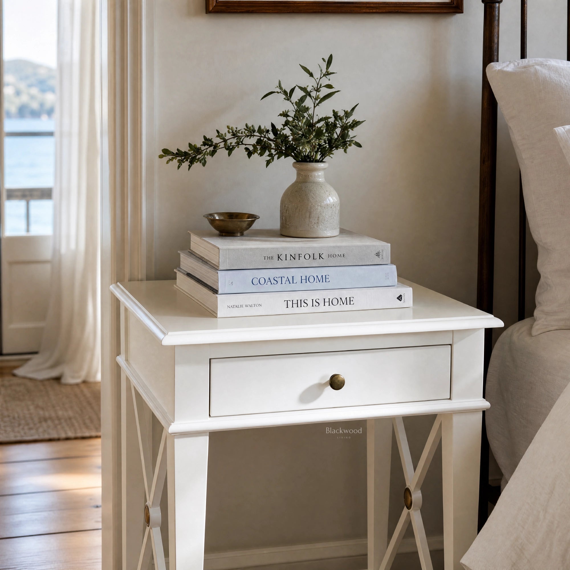 Harbour Bedside Table in white solid poplar, with books and a ceramic vase of greenery on top.