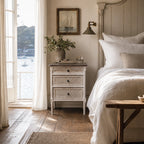 Laguna Bedside Table in distressed white with wicker drawers beside a bed in a coastal, Hampton-inspired bedroom.