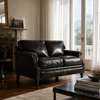 Belgravia 2-seat Estate Black leather sofa in a sunlit living room with curtains and fireplace