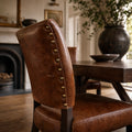 Beaumont Dining Chair in Vintage Tobacco leather with brass nailhead trim in warm dining room.