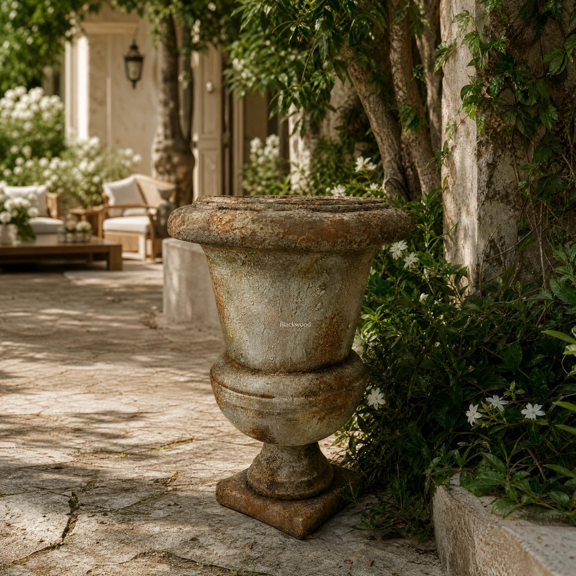 Provence Urn, antique marble-look magnesia composite, weathered finish, set in a sunlit stone courtyard with ivy.