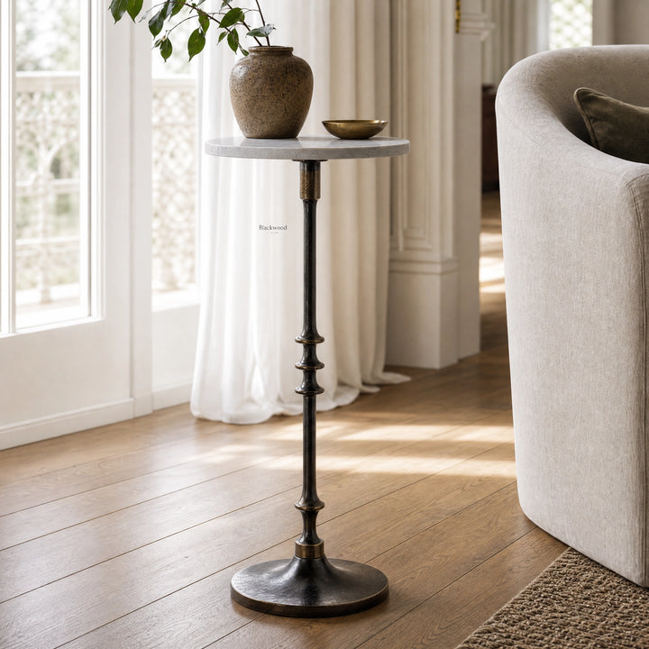 Mayfair Marble Side Table with white marble top and black iron pedestal beside a brass bowl and vase in a living room.