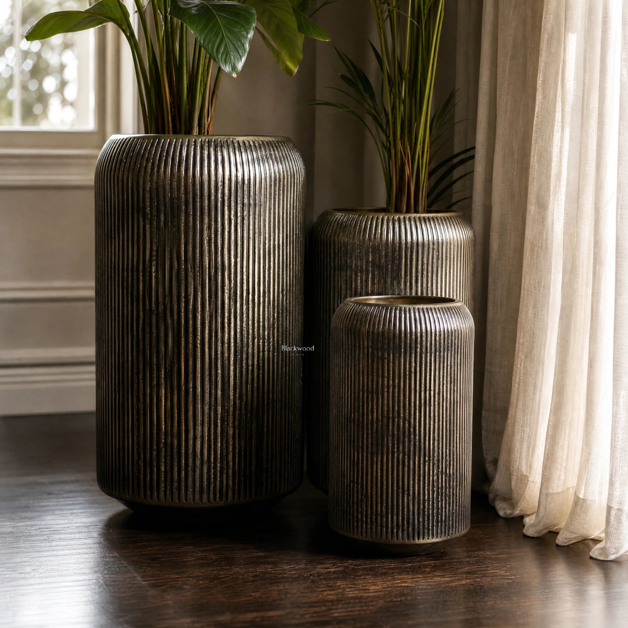 Sumatra Planters Set/3: three aluminium planters in antique brass with ribbed surface and greenery indoors.