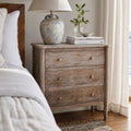 Saltwood Bedside Table in washed oak with weathered finish and ridged detailing, beside bed with lamp and stacked books
