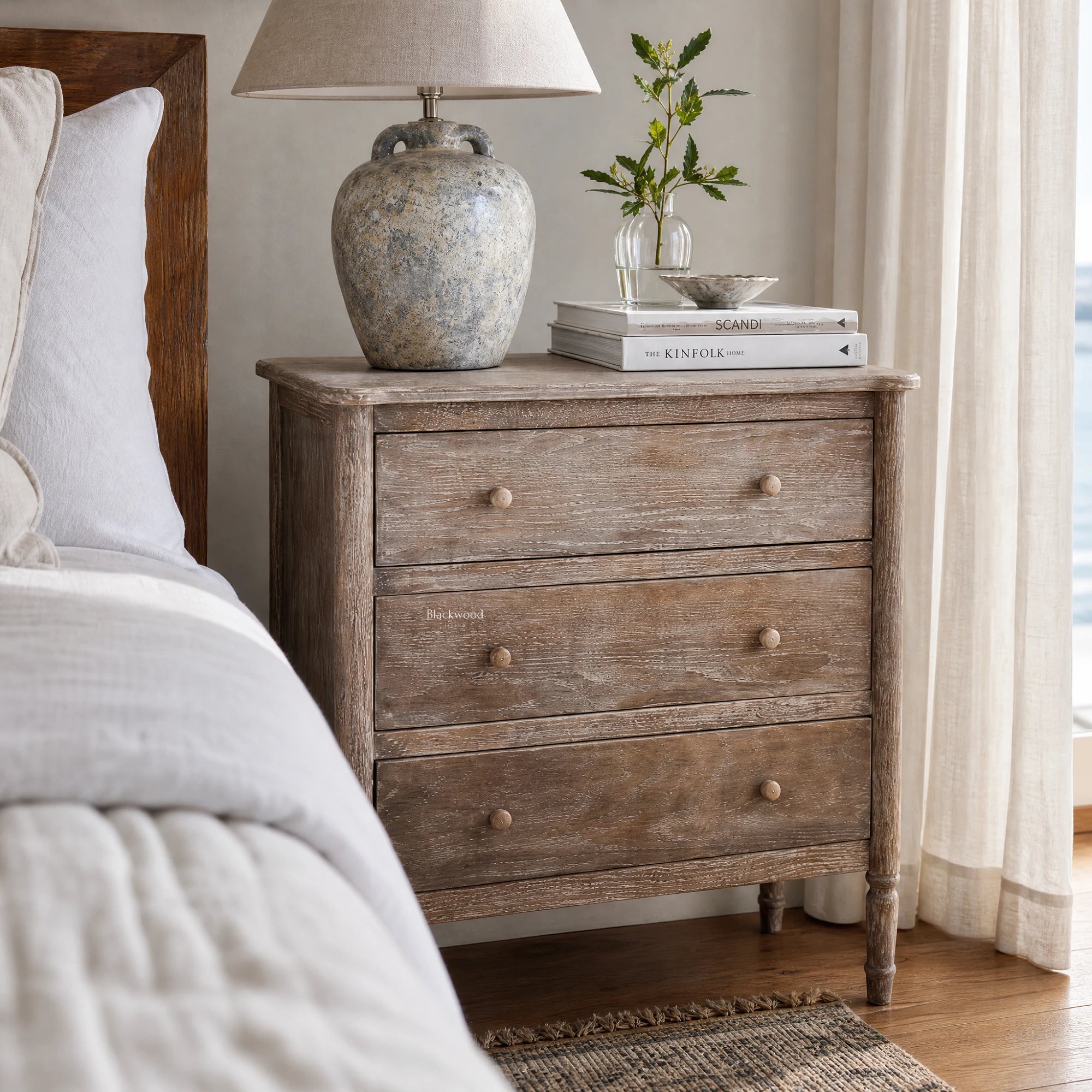 Saltwood Bedside Table in washed oak with weathered finish and ridged detailing, beside bed with lamp and stacked books
