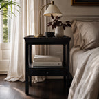 Colombo Bedside Table in a dark alder finish with lamp, vase and books in a neutral bedroom.