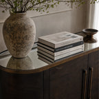 Meridian Sideboard with mirrored top, rustic vase and travel books on a dark wood cabinet.