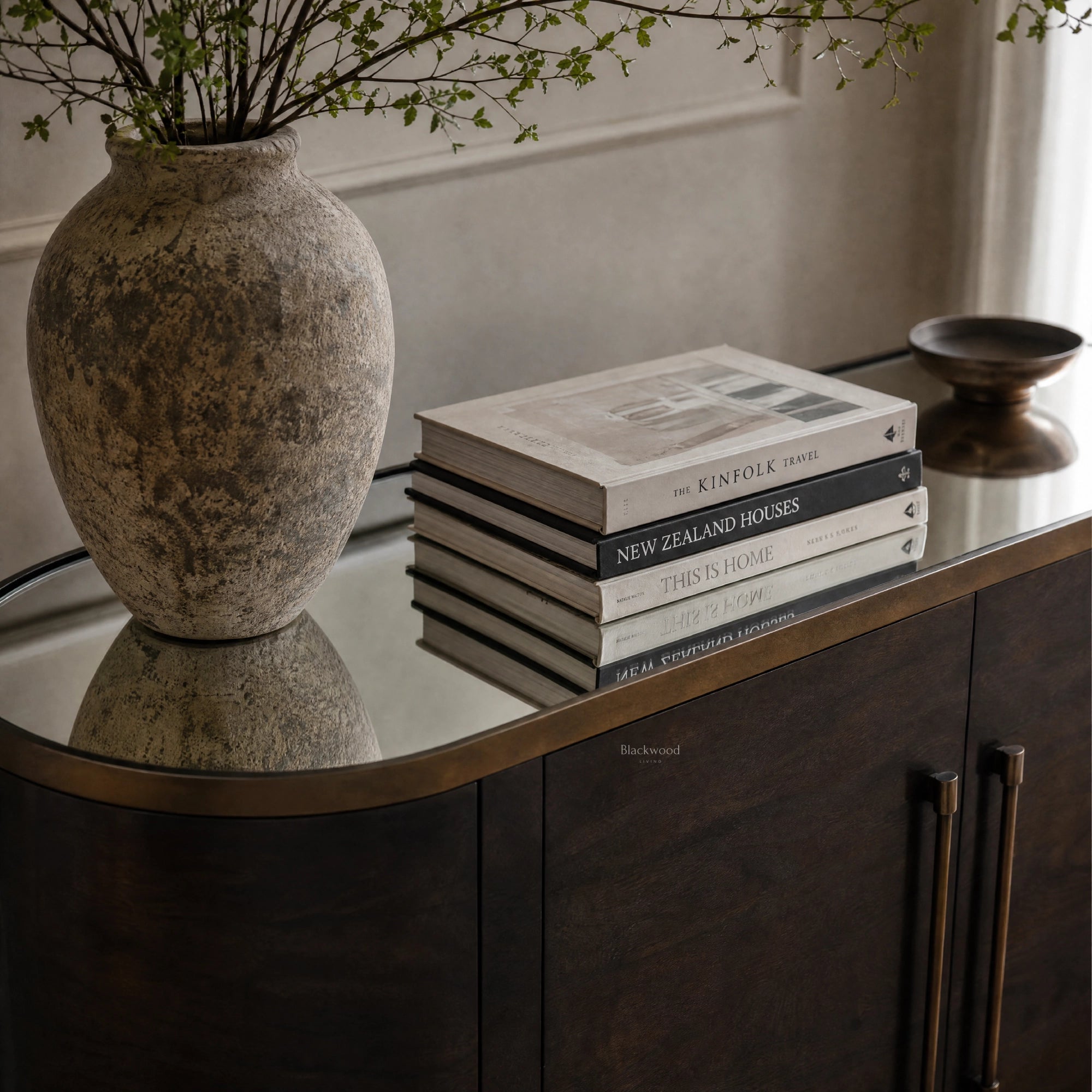 Meridian Sideboard with mirrored top, rustic vase and travel books on a dark wood cabinet.