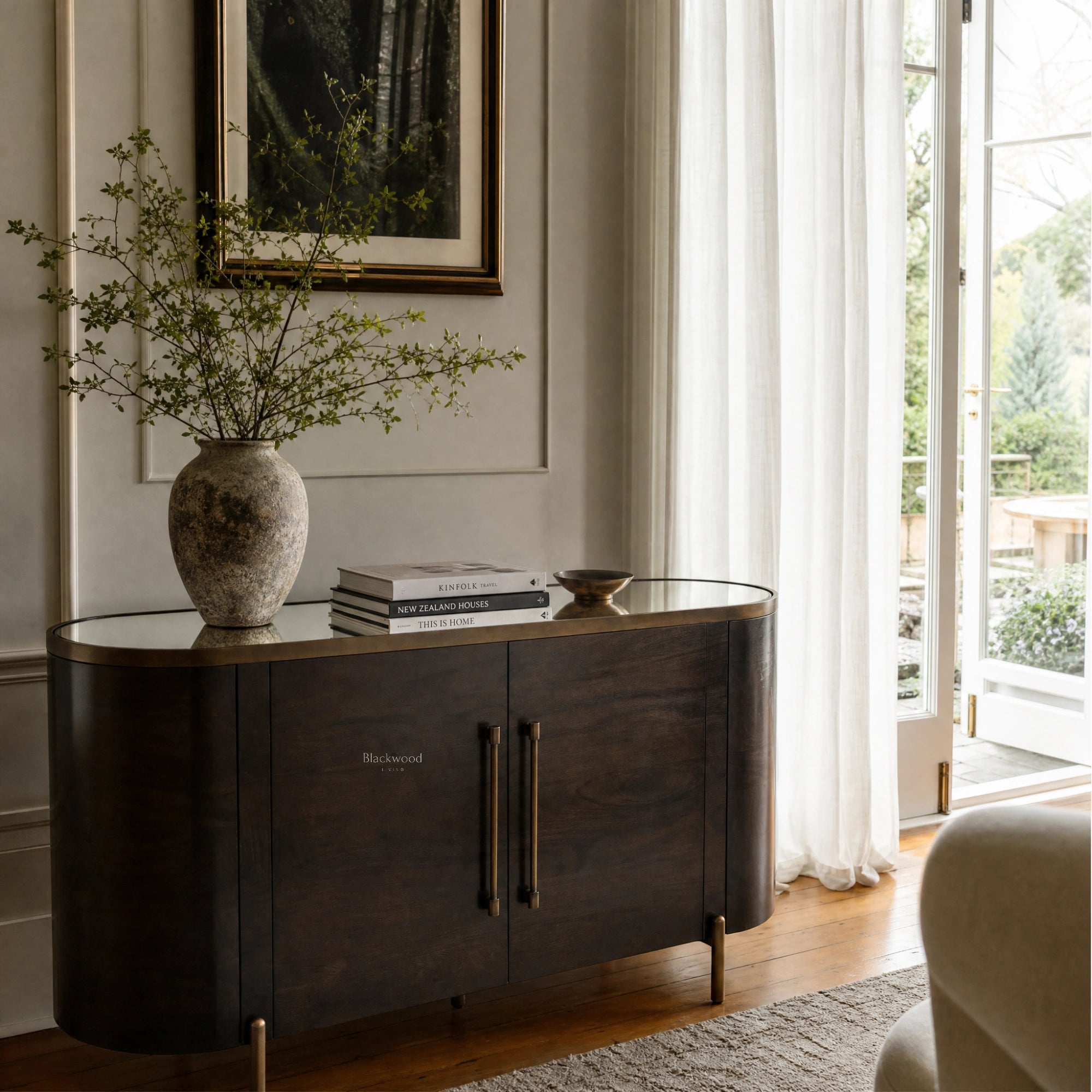 Meridian Sideboard in dark mango wood with brass accents and curved silhouette in a sunlit living room.