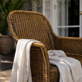 Malacca Accent Chair in woven natural rattan with curved arms and high back, cream throw draped.