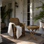 Malacca Accent Chair in natural woven rattan with curved arms and high back on a sunlit porch.