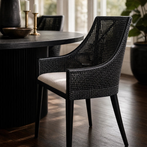 Barbados Dining Chair: black woven rattan with curved back and arms, cream seat cushion in dining room.