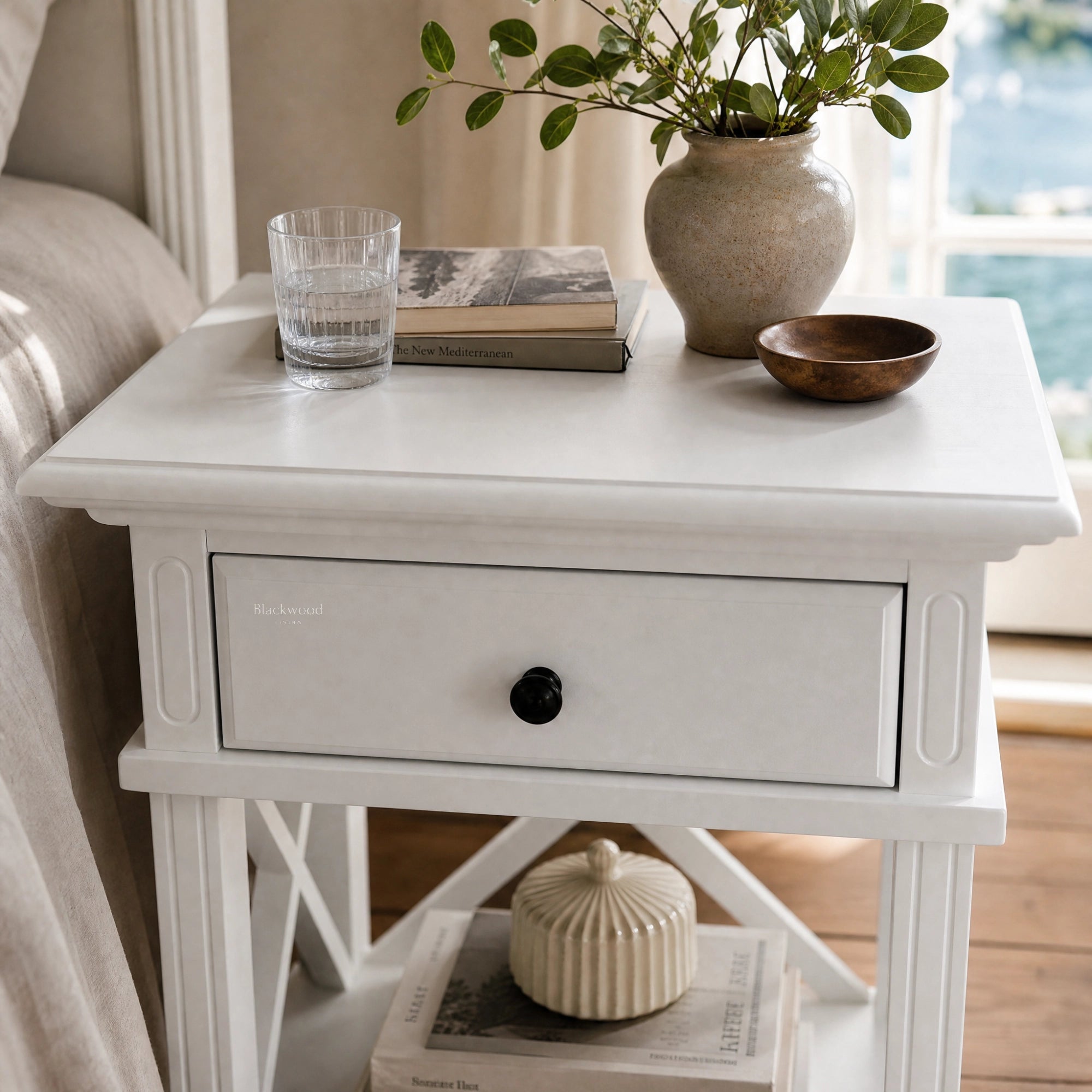 Bridgeport 1 Drawer Bedside - White with black knob, styled with vase, books, and glass on a white table.
