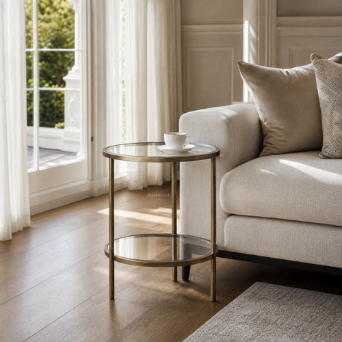 Belgrave Side Table - Brass: brass-finished iron frame with two clear glass surfaces beside a beige sofa.