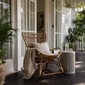 Sika Originals Monet Rattan Rocking Chair on a verandah, with greenery and white-framed doors.