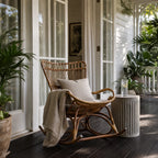 Sika Originals Monet Rattan Rocking Chair on a verandah, with greenery and white-framed doors.