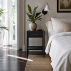 Rangoon Bedside Table - Black in a bright modern bedroom with a plant, wall lamp, and framed art.