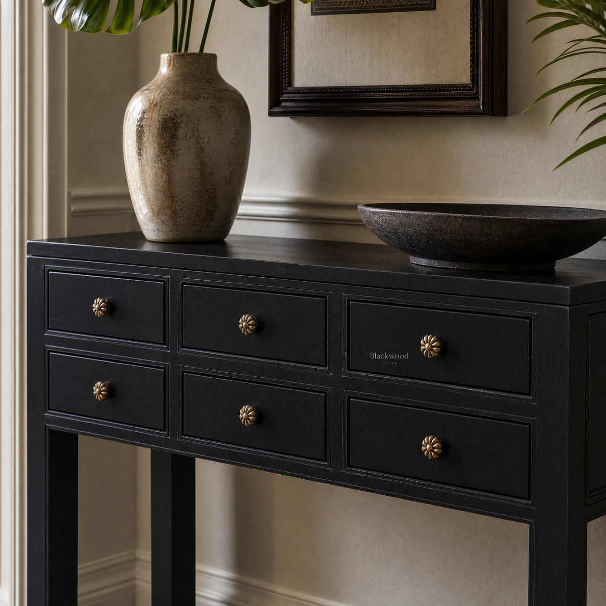 Black 6-drawer hall table with slender legs and antique bronze flower handles, styled with a ceramic vase and dark bowl.