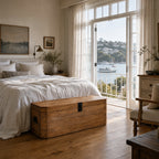 Reclaimed elm trunk with simple metal hardware placed at the foot of a bed in a bright, nautical bedroom overlooking the water.
