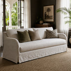 Monique Linen Slipcover Sofa with a full-length skirt and textured linen, neutral cushions in a sunlit living room.
