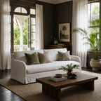 White linen slipcover sofa with curved arms and full-length skirt in a moody living room with dark walls and sheer curtains.
