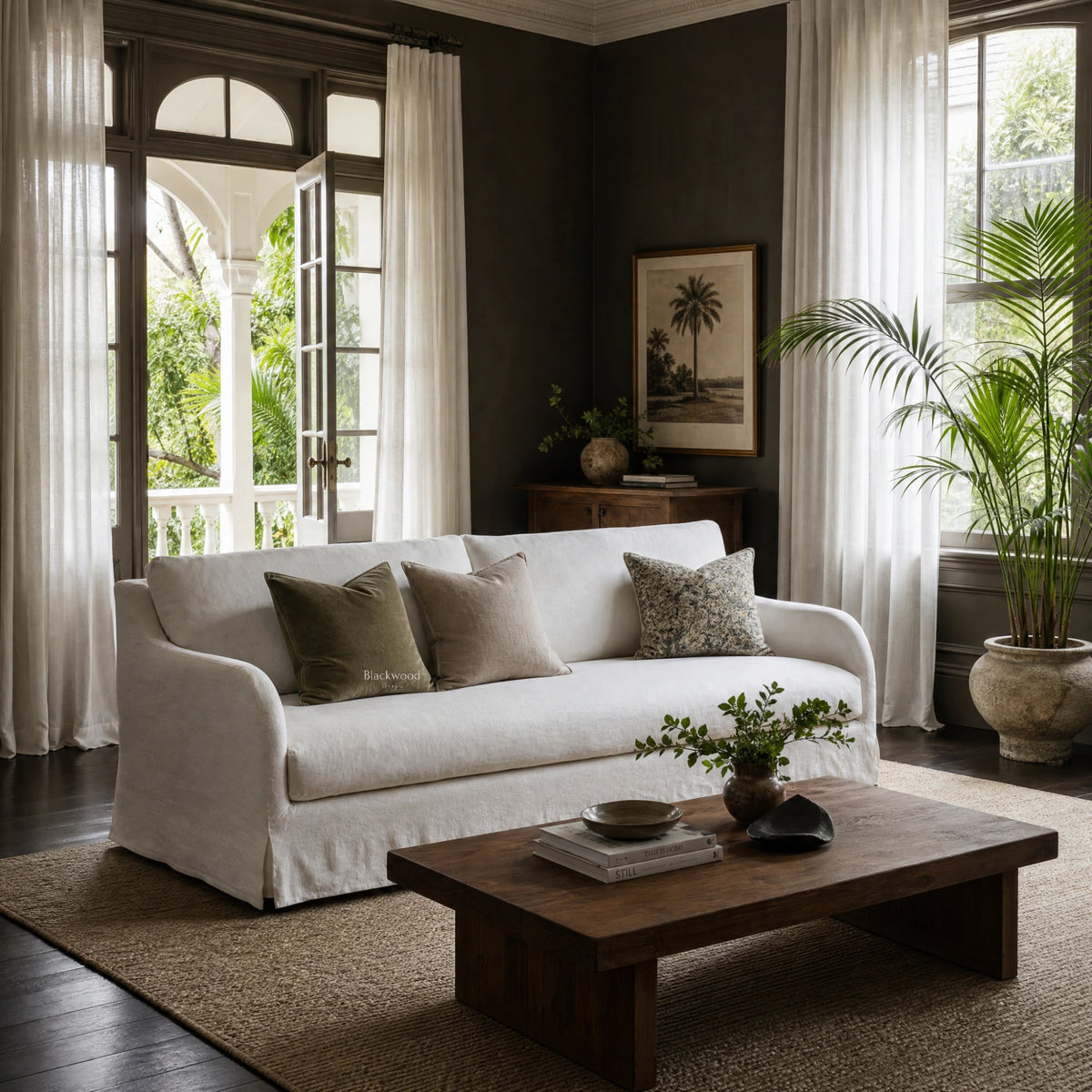 White linen slipcover sofa with curved arms and full-length skirt in a moody living room with dark walls and sheer curtains.