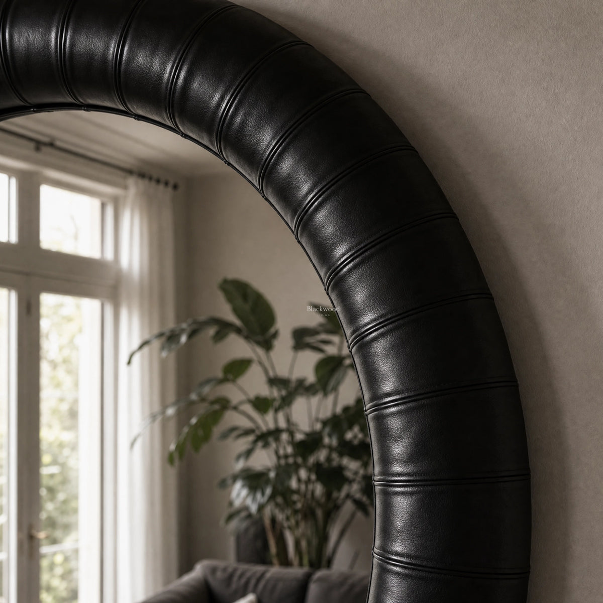 Round mirror with thick, panelled ebony leather frame featuring rich texture and substantial character in a tailored interior setting.