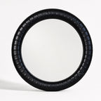 Round mirror with a thick, ribbed ebony leather frame featuring subtle panelled detailing for a crafted, substantial look.