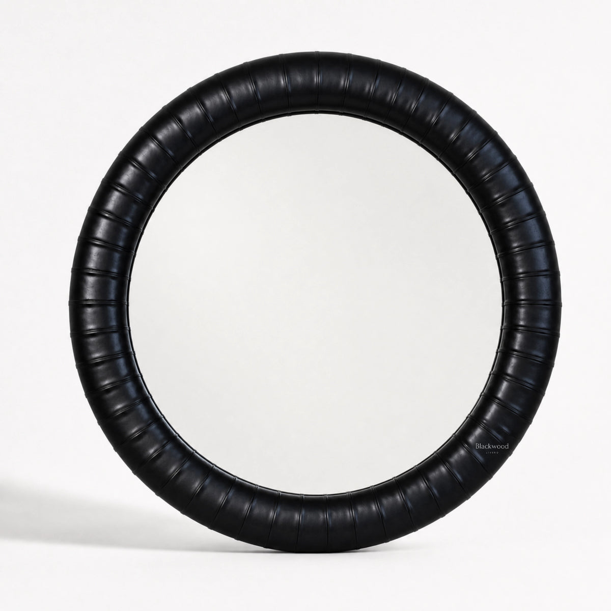 Round mirror with a thick, ribbed ebony leather frame featuring subtle panelled detailing for a crafted, substantial look.