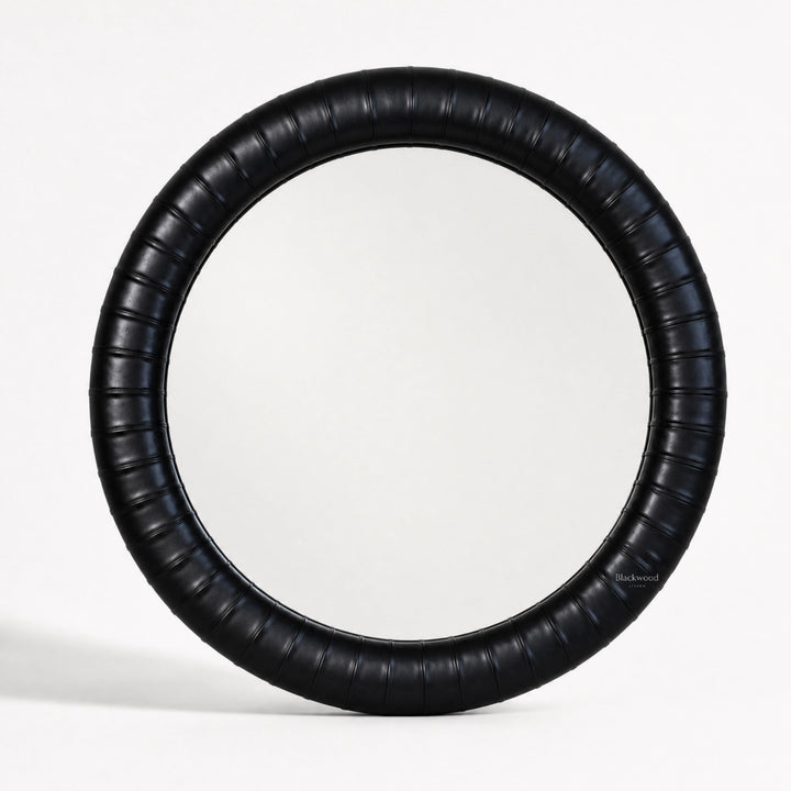 Round mirror with a thick, ribbed ebony leather frame featuring subtle panelled detailing for a crafted, substantial look.