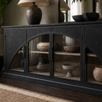 Dark archway sideboard with sweeping arched glass doors, warm timber interior, and ceramic vases displayed on shelves.