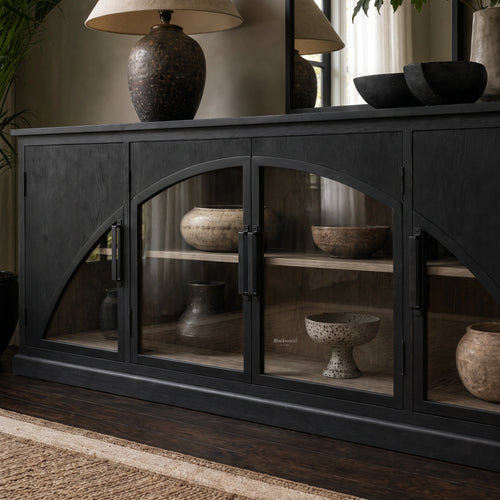 Dark archway sideboard with sweeping arched glass doors, warm timber interior, and ceramic vases displayed on shelves.