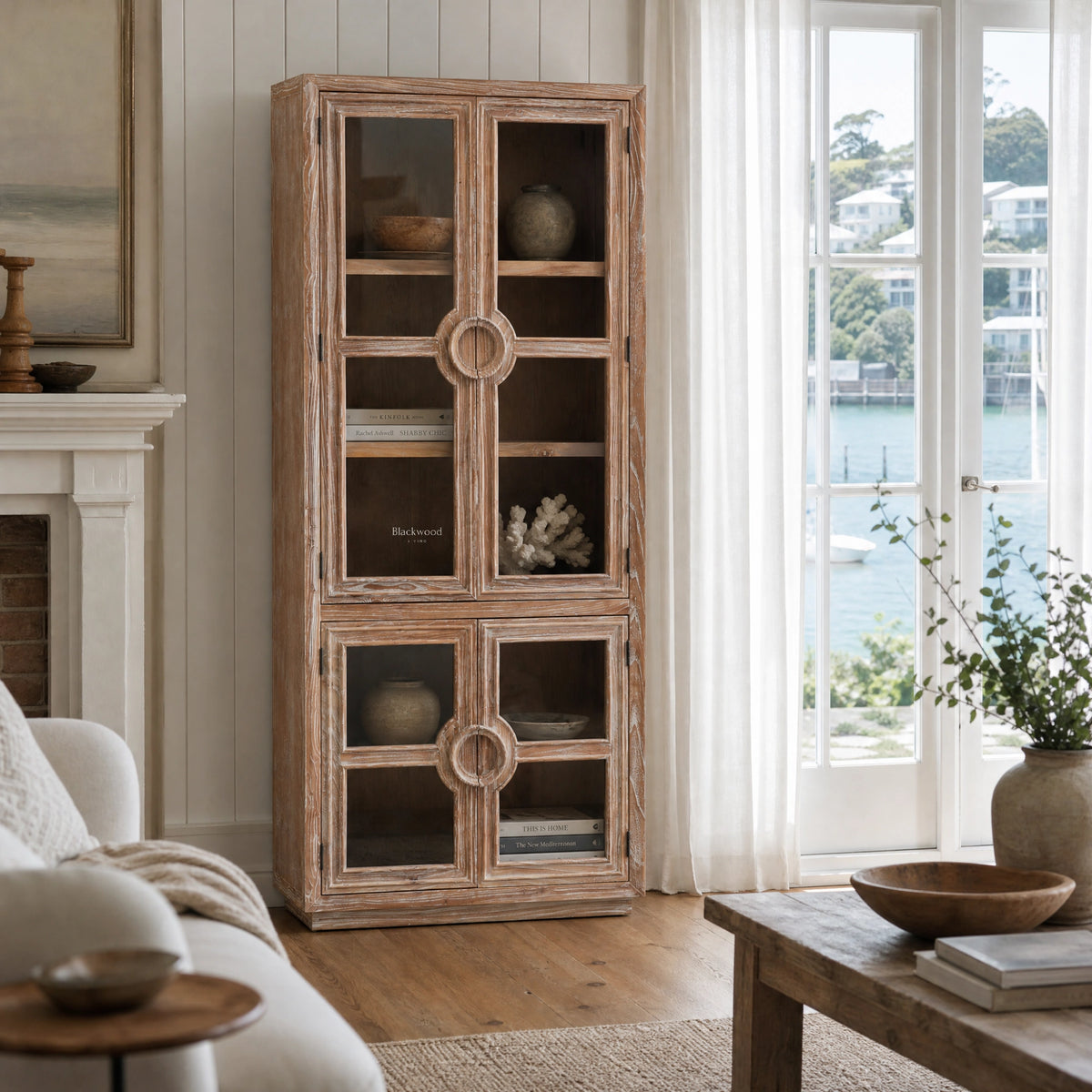 Tall distressed elm Capstan Cabinet with glazed doors and nautical circular handles adding coastal character to a bright living room.