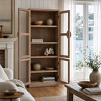 Tall elm Capstan Cabinet with open glazed doors, circular nautical handles, and shelves displaying books and pottery in a coastal living room.