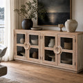 Light elm sideboard with glass doors and circular handles. Coastal style timber furniture styled with ceramics and a seascape painting.