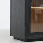 Dark elm sideboard corner featuring arched glazed door frame, visible hinge, and light interior shelving with traditional ecclesiastical detailing.