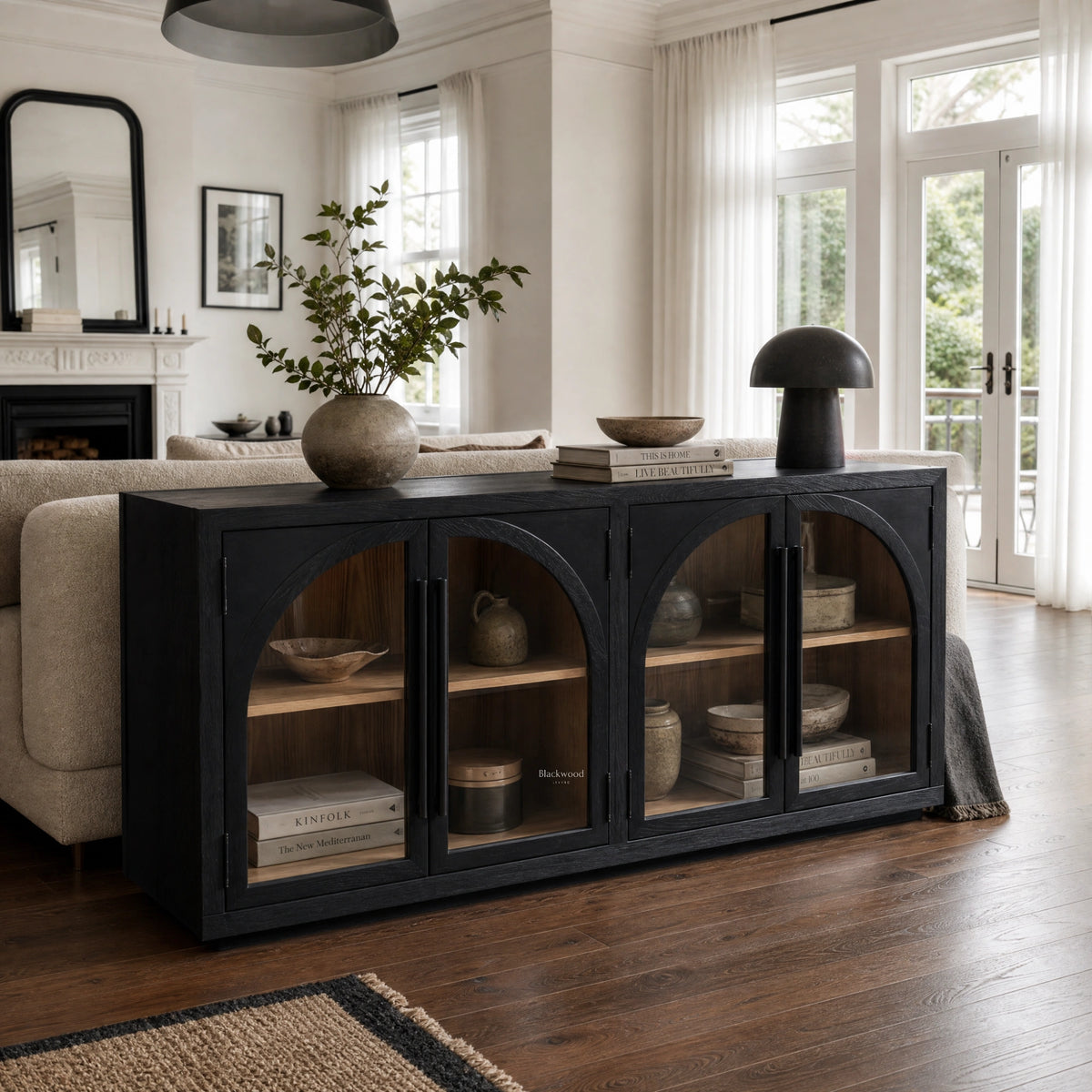 Dark elm sideboard with four glazed doors featuring graceful arched detailing, styled behind a sofa in a bright living room.